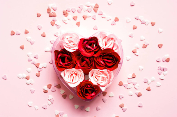 Valentines Day. Heart shape formed of roses flower petals on pink background with sweet confetti. Festive concept - Photo, Image