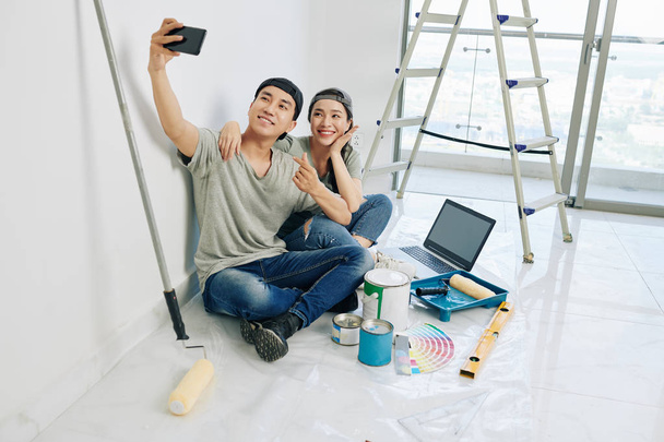 glückliche junge vietnamesische Paar posiert für Selfie mit Werkzeugen und Farben vor der Renovierung Haus - Foto, Bild