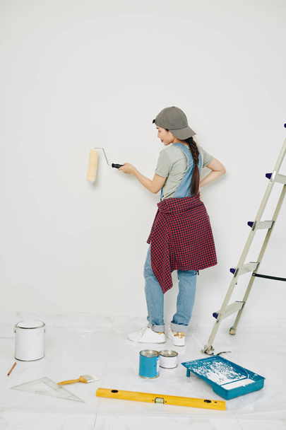 Pretty young Asian woman enjoying painting walls in her new apartment with roller - Foto, immagini