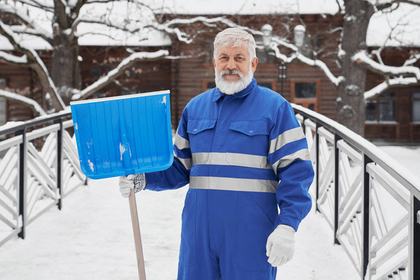 Positive bearded man holding shovel in hand in winter - 写真・画像