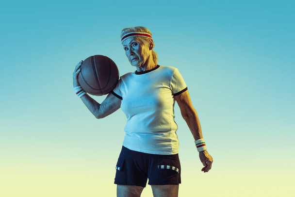 Senior woman playing basketball in sportwear on gradient background in neon light - Fotó, kép