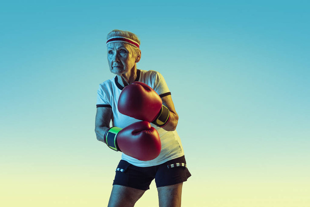 Senior woman boxing in sportwear on gradient background in neon light - Fotoğraf, Görsel