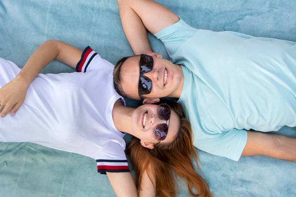 Молодая пара подростков в солнечных очках, лежащих вместе на голубой ткани
 - Фото, изображение