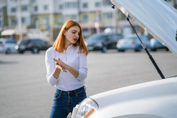 Young stressed woman driver standing near broken car with open h - Photo, Image