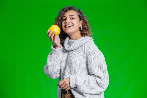 Young beautiful girl, with curly hair and toothy smile, holds a big yellow apple to enjoy the taste. - Foto, immagini