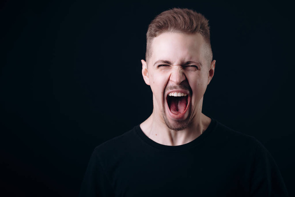 Young Man in Black Screaming With His Eyes Squinted - Фото, изображение