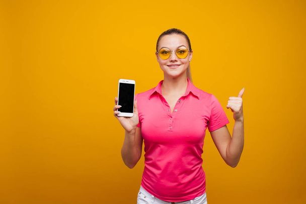 Bright and cheerful young woman in a pink t-shirt on a yellow background. - Foto, Bild
