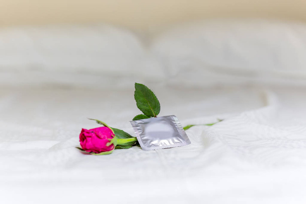 Prezerwatywa i kwiat róży na łóżku. - Zdjęcie, obraz