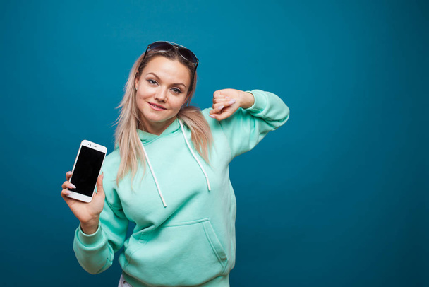 Stylish trendy hipster girl in the blue hoodie with the hood uses a smartphone. - Foto, Imagen