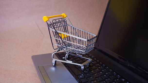 Koop nu, Shopaholic op het internet. Online winkelen, winkelwagen op laptop toetsenbord. - Foto, afbeelding