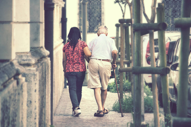 уход за престарелыми в городе, женщина сопровождает старика
 - Фото, изображение