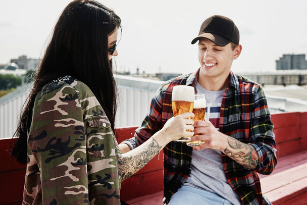 Onnellinen hymyilevä pari paahtaminen ja oluen juominen ulkona pubissa tai baarissa katolla kesällä
 - Valokuva, kuva