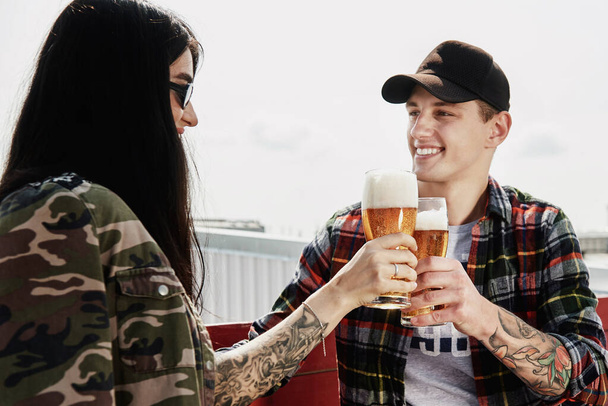 Happy smiling couple toasting and drinking beer at outdoor pub or bar on rooftop at summer - Foto, Bild