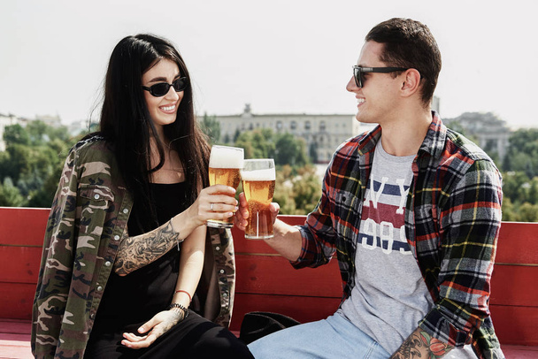 Šťastný usměvavý pár přípitek a pití piva v venkovní hospodě nebo baru na střeše v létě - Fotografie, Obrázek