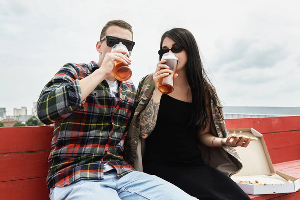 Happy smiling couple drinking beer and eating pizza at outdoor pub or bar on roof, copy space - Foto, imagen