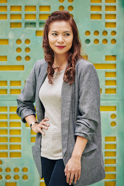 Positiva mujer asiática confiada sonriendo y mirando hacia otro lado al estar al aire libre
 - Foto, imagen