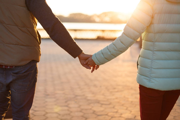 Közelről láthatjuk, ahogy fiatal szerelmesek fogják egymás kezét. Szülők babakocsival az őszi parkban. Szerelem, szülőség, család, évszak és emberek fogalma. - Fotó, kép