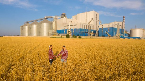 People shaking hands in a wheat field, farmers agreement. Grain elevator terminal on background. Agriculture agronomist business contract concept. Aerial photo. Agriculture theme - Фото, зображення