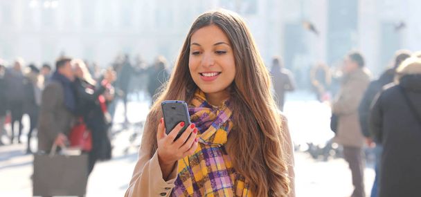 Uśmiechnięta młoda kobieta czytająca wiadomości przez telefon komórkowy dowcip na zewnątrz - Zdjęcie, obraz