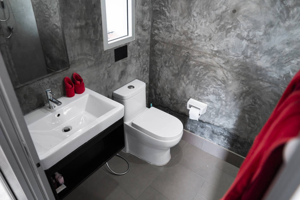 Ev banyosunda lavabosu ve duvarında gri kiremitleri olan kırmızı havluları olan beyaz bir tuvalet ve duvarında da tuvalet kağıdı var. Banyo lüks iç mekan.. - Fotoğraf, Görsel