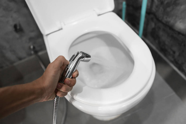 Using of bidet shower with a white toilet. Bidet shower in male hand for using with a white toilet bowl. - Foto, Imagen