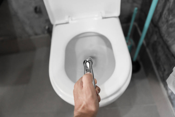 Using of bidet shower with a white toilet. Bidet shower in male hand for using with a white toilet bowl. - Fotoğraf, Görsel