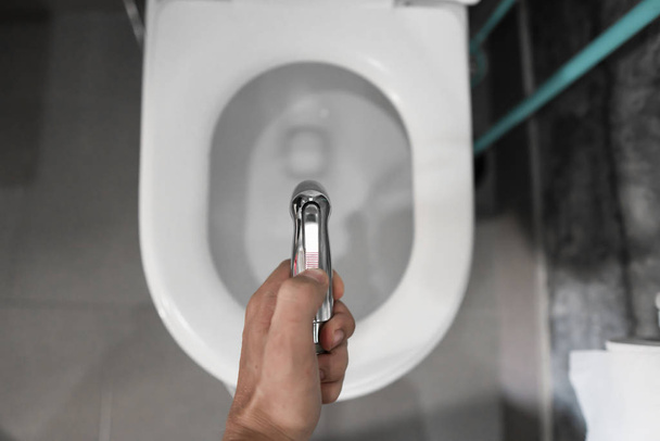 Using of bidet shower with a white toilet. Bidet shower in male hand for using with a white toilet bowl. - Фото, изображение