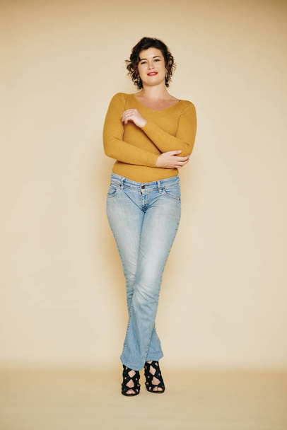 Foto tiro de mulher bonita positiva em jeans e salto alto posando em estúdio
 - Foto, Imagem