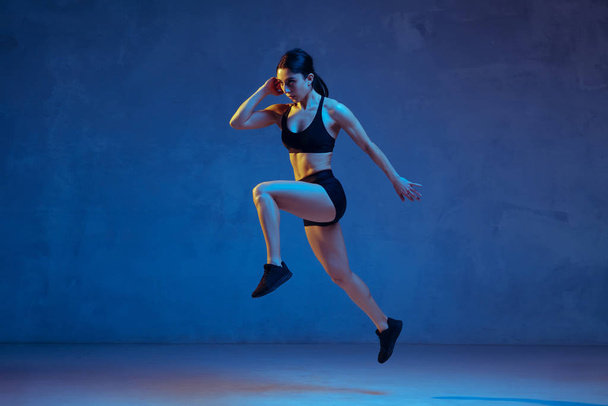 Caucasian young female athlete practicing on blue studio background in neon light - Foto, Bild