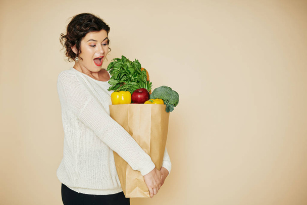 Feliz dona de casa animado olhando para grande saco de supermercado pesado em suas mãos
 - Foto, Imagem