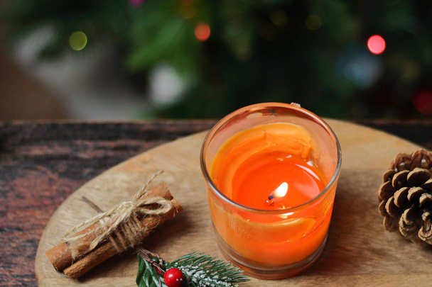 Beautiful Christmas orange mandarin candle on a wooden stand with sticks of whole cinnamon, sprig of mistletoe and a Christmas tree decorated with toys. Christmas New year evening mood, greeting card - Fotó, kép