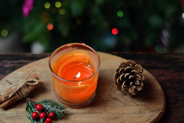 Bela vela de tangerina laranja de Natal em um suporte de madeira com paus de canela inteira, raminho de visco e uma árvore de Natal decorada com brinquedos. Natal clima da noite de ano novo, cartão de saudação
 - Foto, Imagem