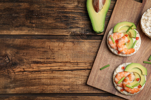 Puffed rice cakes with shrimps and avocado on wooden table, flat lay. Space for text - Foto, Imagen
