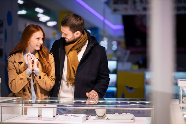 redhaired woman with male selects expensive jewelry at jewelers shop - Фото, изображение