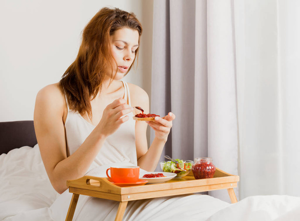 Young woman having breakfast in the hotel bed. - Photo, image