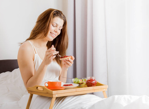 Young woman having breakfast in the hotel bed. - Fotoğraf, Görsel
