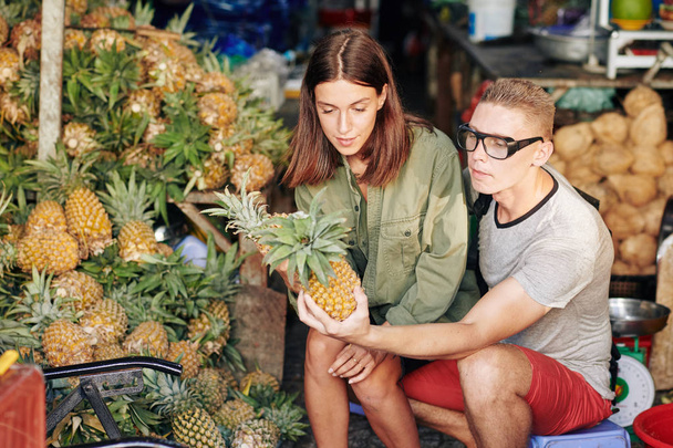 Joven pareja caucásica eligiendo piñas frescas en el mercado local
 - Foto, imagen