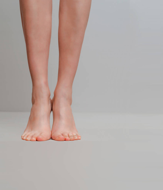 Λεπτές γυναικεία πόδια που υψώνονται στα δάχτυλα των ποδιών σε ανοιχτό γκρι φόντο - Φωτογραφία, εικόνα