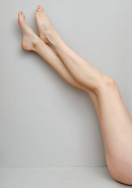 Slender legs of a woman bent to her knees on a gray background - Photo, Image