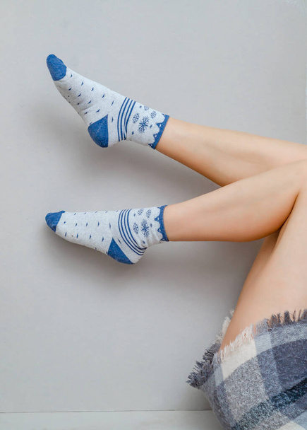 Λεπτά πόδια μιας γυναίκας με κάλτσες λυγισμένες στα γόνατά της σε γκρι φόντο. - Φωτογραφία, εικόνα