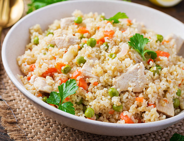 Bulgur with chicken, green peas and carrot  on wooden background. - Fotó, kép