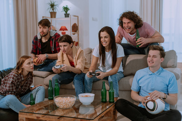 Grande grupo de amigos em grande espaçosa sala de estar assistindo a um jogo na frente da TV muito animado e concentrado eles sentam-se no sofá
 - Foto, Imagem