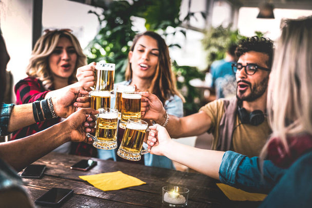 Друзья пьют пиво в пивоваренном баре в помещении на вечеринке на крыше - Концепция дружбы с молодыми людьми, веселящимися вместе, выпивая в акцию "Счастливый час" - Сосредоточьтесь на очках - Теплый виньетирующий фильтр
 - Фото, изображение