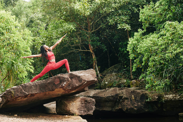 Bonita deportista negra en top rojo brillante y leggins practicando la pose guerrera de dos
 - Foto, imagen
