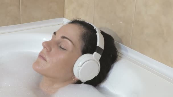 Nő vesz egy buborék fürdő fürdőszobában otthon, és visel fejhallgatót.Vezeték nélküli szabadság Bluetooth technológia koncepció - Felvétel, videó