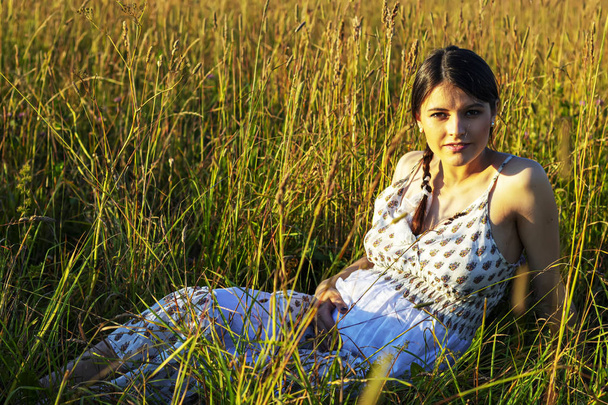A young Caucasian pregnant girl lies in the grass. The concept of unity with nature - 写真・画像