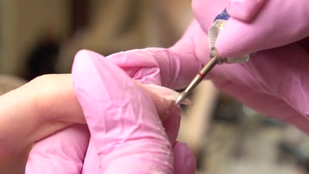 Close-up shot of hardware manicure in a beauty salon. Manicurist is applying electric nail file drill for trim cuticles on female fingers - Footage, Video