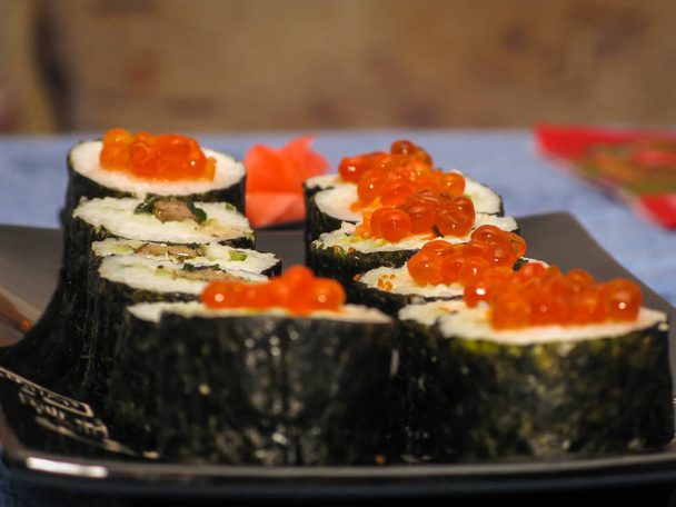 sushi zdobené červeným kaviárem na černém tradičním talíři - Fotografie, Obrázek