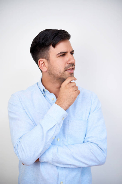 Portrét zamyšleného mladého podnikatele v světle modré košili dotýkajícího se brady a odvracejícího se pohledu - Fotografie, Obrázek