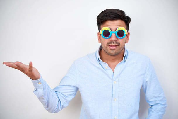 Jovem empresário em engraçado plástico crianças óculos de sol encolher ombros e fazer gesto de mão
 - Foto, Imagem